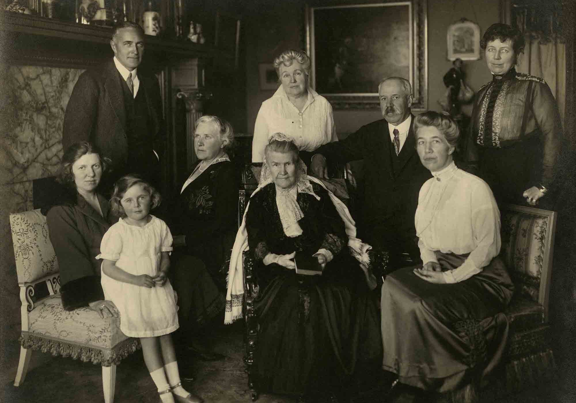 "Bourn family portrait taken at 2050 Broadway, S.F.  Sarah Esther Chase Bourn, seated in ornate arm chair, in dark long dress with light-colored shawl over her shoulders, full light-colored lace scarf tied at her neck, white lace mantilla on the back part of her head, surrounded by her family.  First row, left to right:  Maud Bourn Vincent, Elizabeth Rose Vincent, Sara Esther Chase Bourn, Maude Bourn Hayne.  Second row, left to right: Arthur Rose Vincent, Agnes Moody Bourn, Maye Bourn Tucker, William Bowers Bourn II, Ida Hoxie Bourn. Sarah Chase Bourn, seated in ornate arm chair, in dark long dress with light-colored shawl over her shoulders, full light-colored lace scarf tied at her neck, white lace mantilla on the back part of her head.  Her right hand rests in her lap; her left hand is obscured by a basket and flowers.  Ferrol Egan's book The Last Bonanza Kings identifies as taken March 1919 at 2030 Broadway, San Francisco."